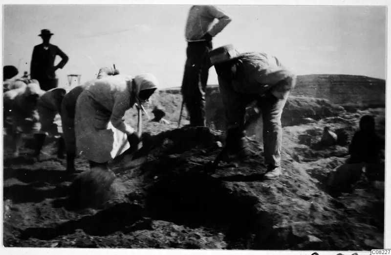 People digging with spades at an excavation, with a mound of loose earth in the foreground