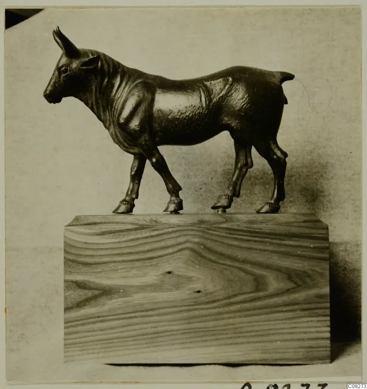 Small bronze figure of a four-legged animal with short upright horns, standing on a wooden block.