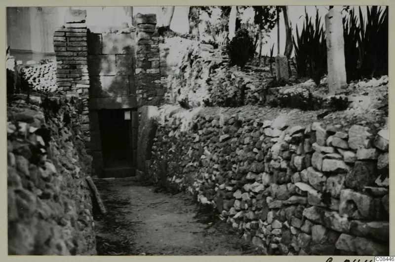 Narrow path between dry-stone walls leading to a doorway in a stone wall