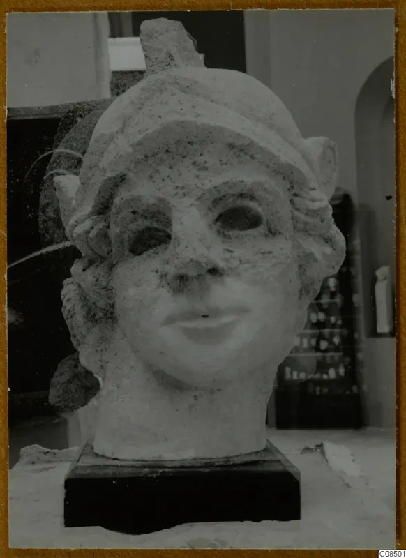 Carved stone head of a figure on a dark base, with wavy hair, a chipped nose and a slight smile