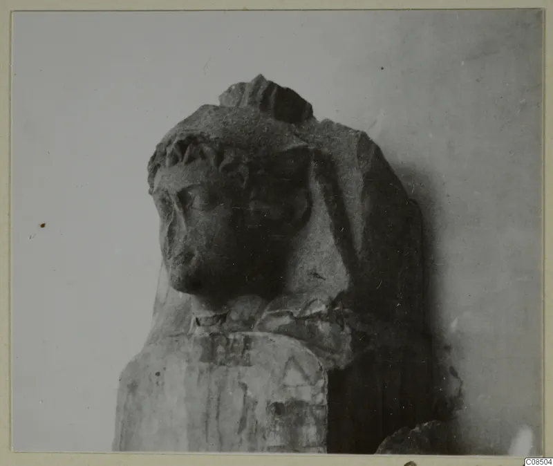 Carved stone head and upper body of a statue, broken at the top and right shoulder, on a rectangular base