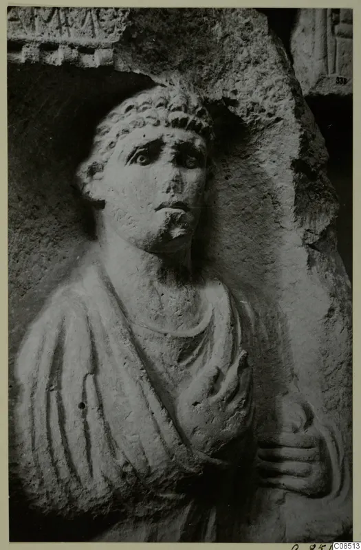 Carved stone figure of a man with curly hair and a short beard, one hand raised to his chest, in North Africa