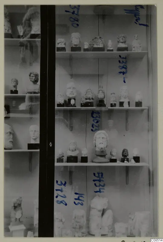Glass display case holding heads, busts and statues on shelves, with blue handwritten numbers on the glass