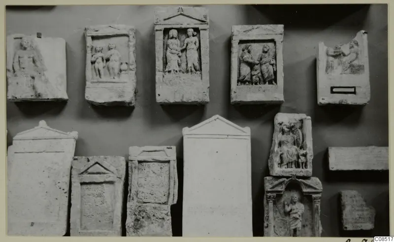 Carved stone slabs and reliefs fixed to a wall in two rows, with standing and seated figures