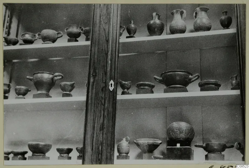 Pottery vessels and bowls on shelves inside a glass-fronted display cabinet