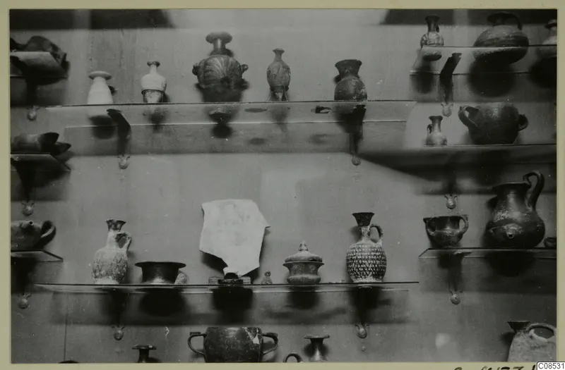 Small jugs, juglets and bowls arranged on wall-mounted shelves in a display case