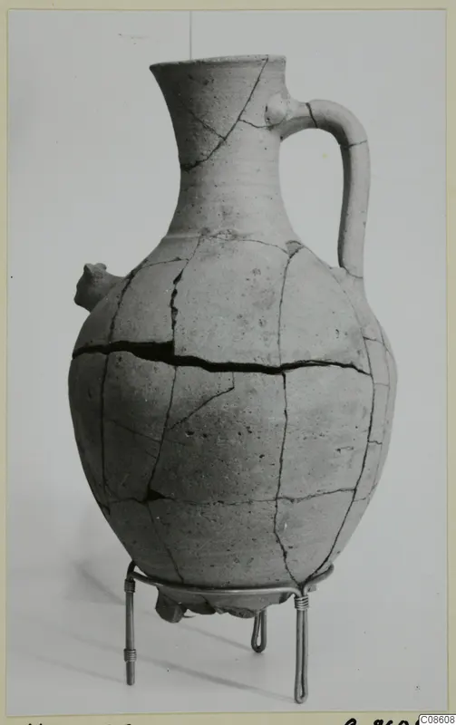 Pottery White Painted VI jug with a loop handle and small spout, standing on a wire stand