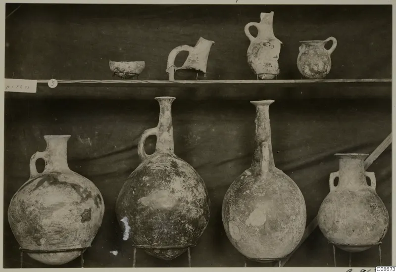 Jugs and a bowl from Lapithos Markides, T.5, set out on two shelves against a dark drape