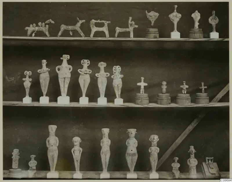 Three shelves of terracotta figurines: small animal figures, standing human figures and stylised idols on bases.