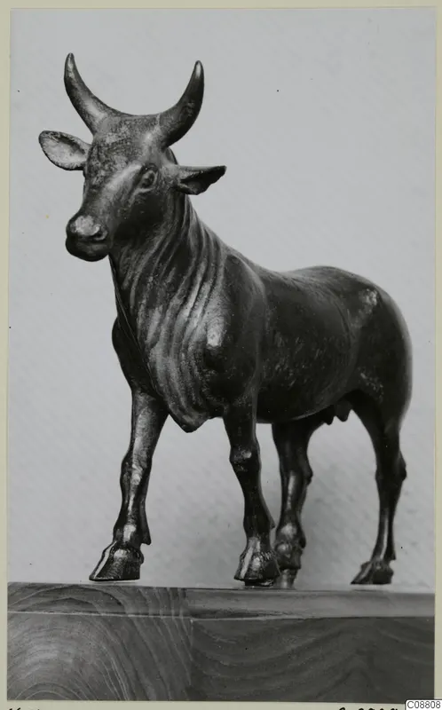 Bronze figure of a standing bull with upswept horns, photographed on a wooden base.