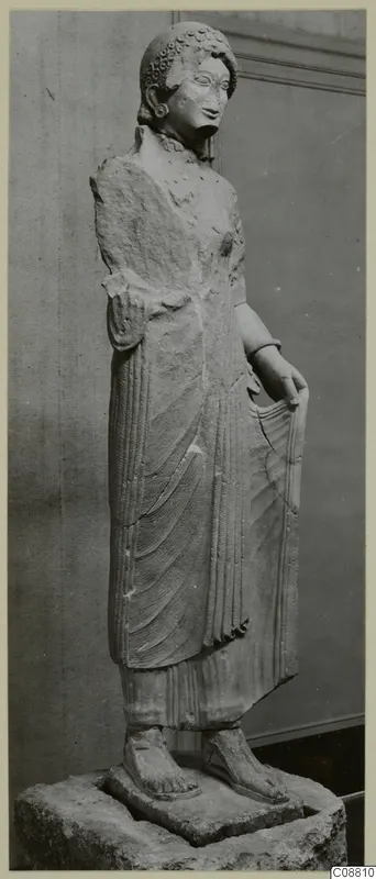 Limestone statue of a standing woman on a stone base, seen from a three-quarter angle.