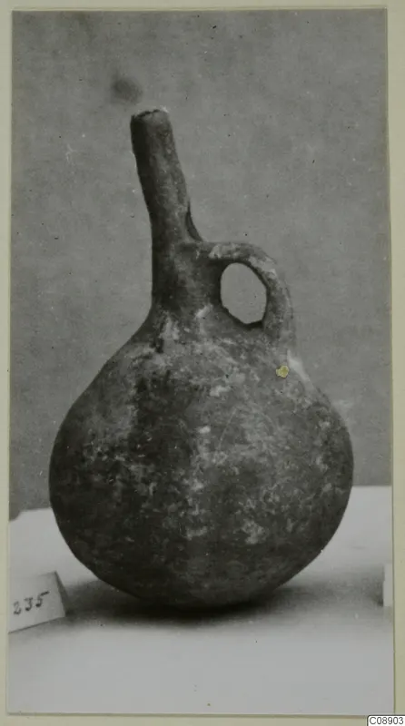 Pottery vessel with a rounded body, long narrow neck and loop handle, photographed on a pale surface
