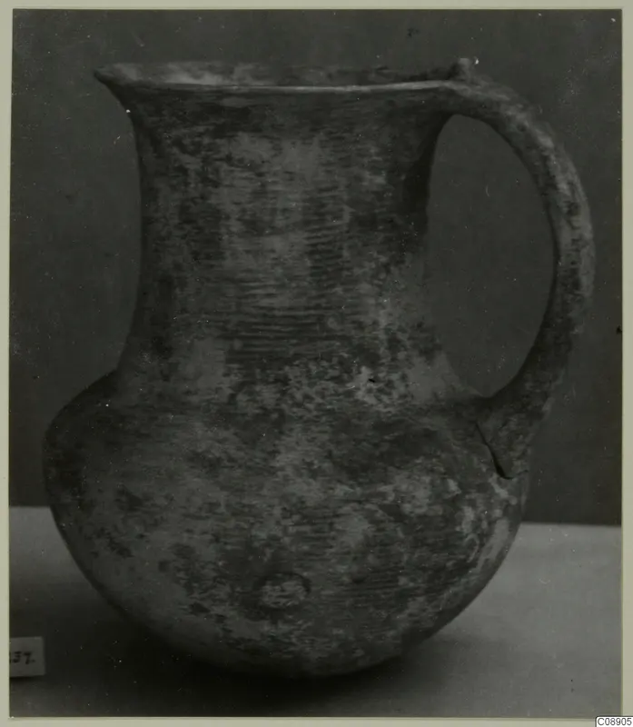 Jug with a flared mouth, a single strap handle and a rounded body, shown against a dark backdrop