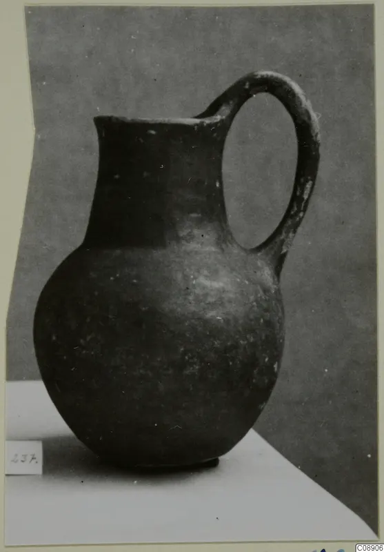 Dark-surfaced jug with a single loop handle, photographed on a pale surface