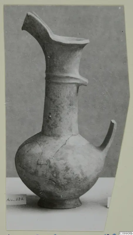 Pottery Base-Ring Ware jug with a flaring spout and a single handle, photographed against a grey backdrop