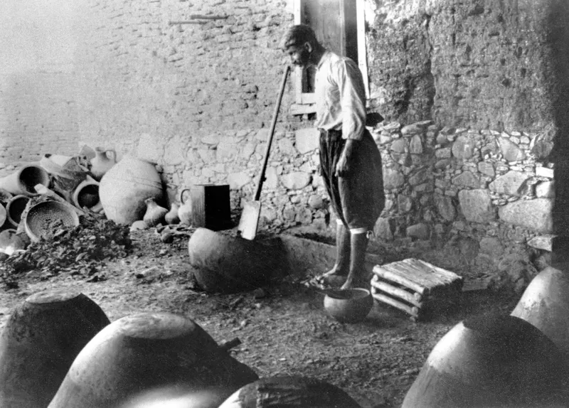 Potter treading clay in a courtyard at Klirou, with large jars and pots around him