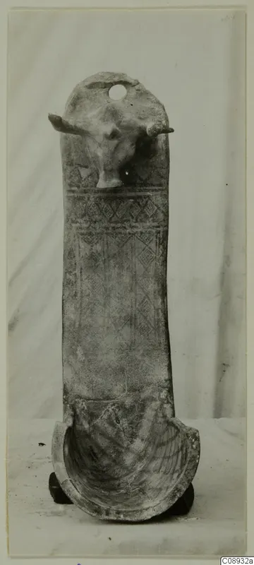 Terracotta object with a modelled animal head with horns at the top and geometric patterns on its tall body