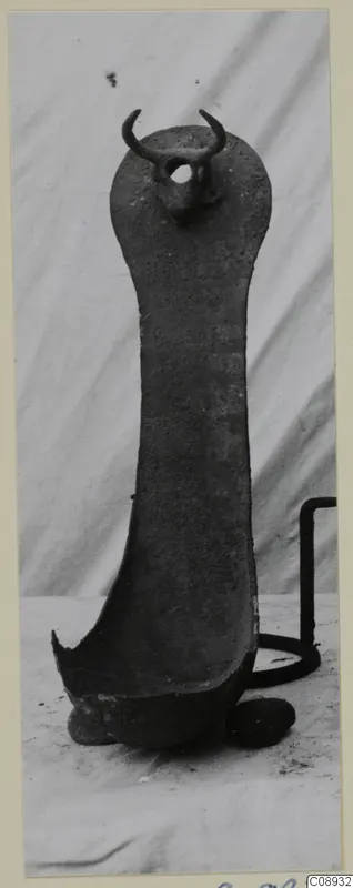 Corroded metal object with a long flat handle, a knob with two curved projections at the top and a shallow bowl-shaped end.