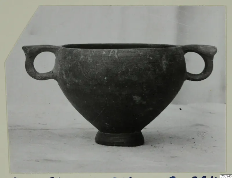 Dark grey two-handled bowl with a short foot, photographed on a light surface against a pale backdrop.