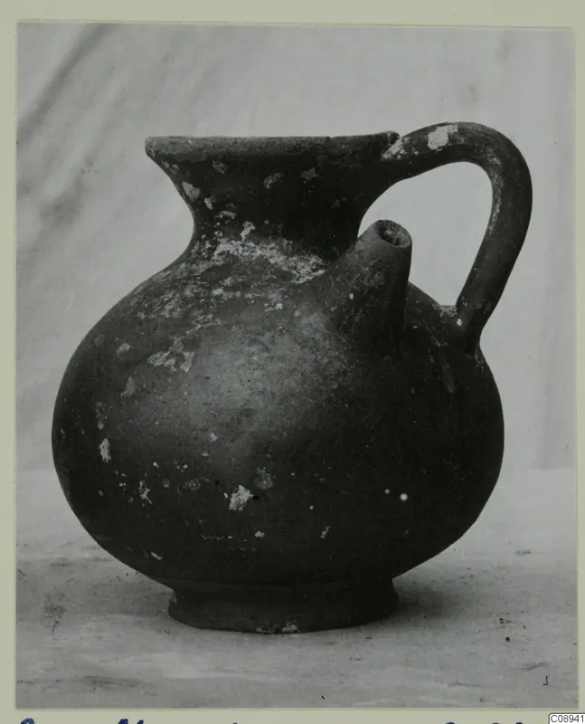 Dark-surfaced jug with a globular body, a side spout and a strap handle.