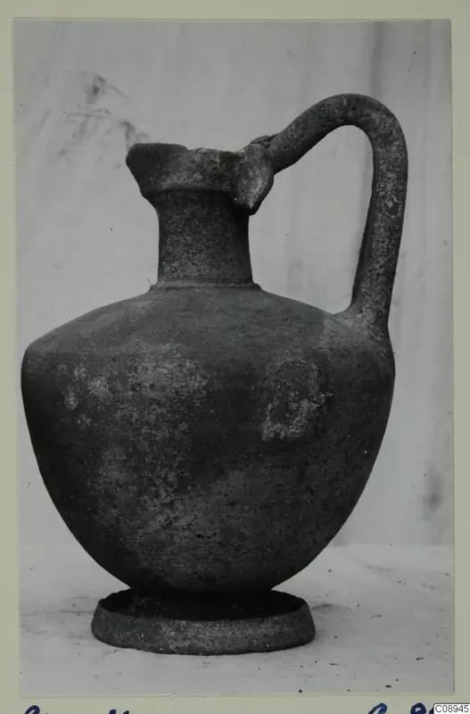 Pottery jug with a single loop handle and ring foot, photographed on a plain backdrop