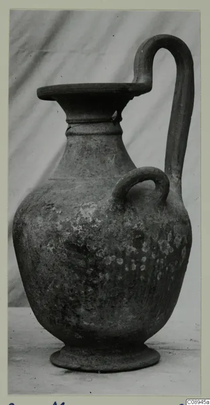 Pottery jug with a tall strap handle, a small loop handle on the body and a wide flat-topped mouth
