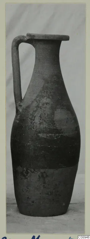 Pottery jug with a single strap handle and a long neck, photographed upright on a card mount