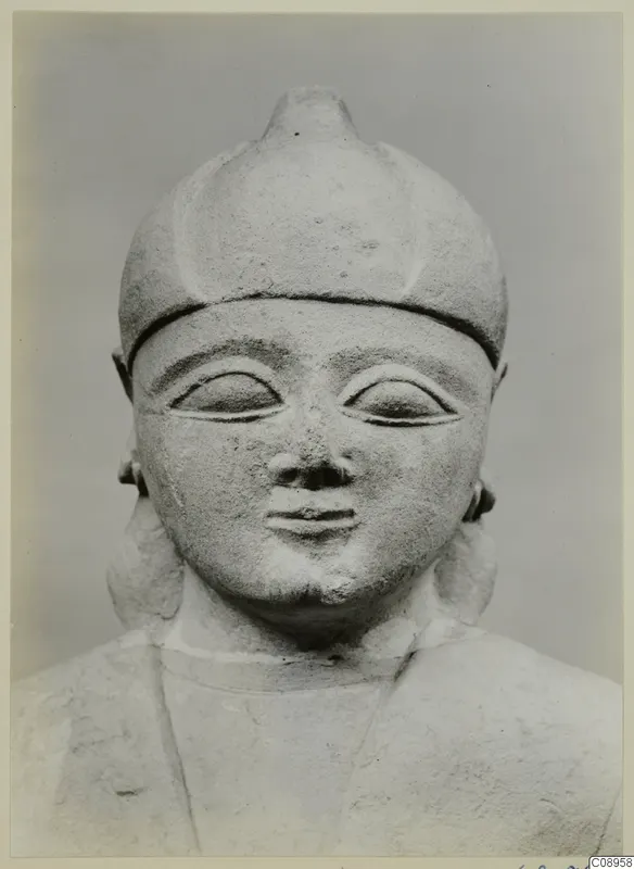 Limestone sculpture of a head and upper body with a rounded, pointed cap and large almond-shaped eyes