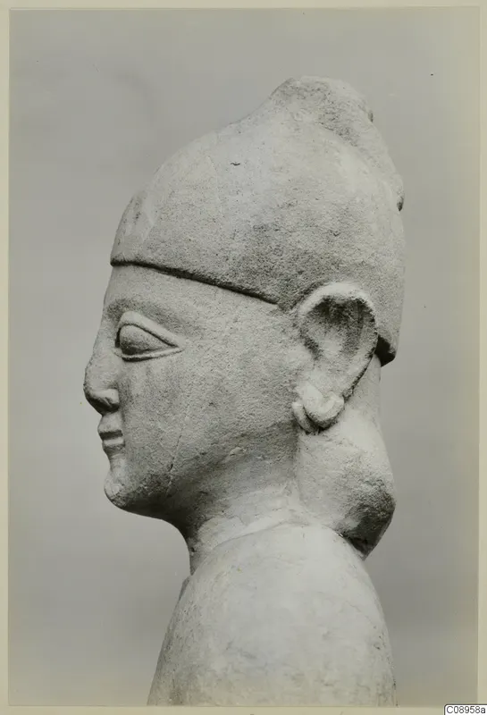 Limestone statue in side profile, head and upper body, wearing a tall cap-like headdress