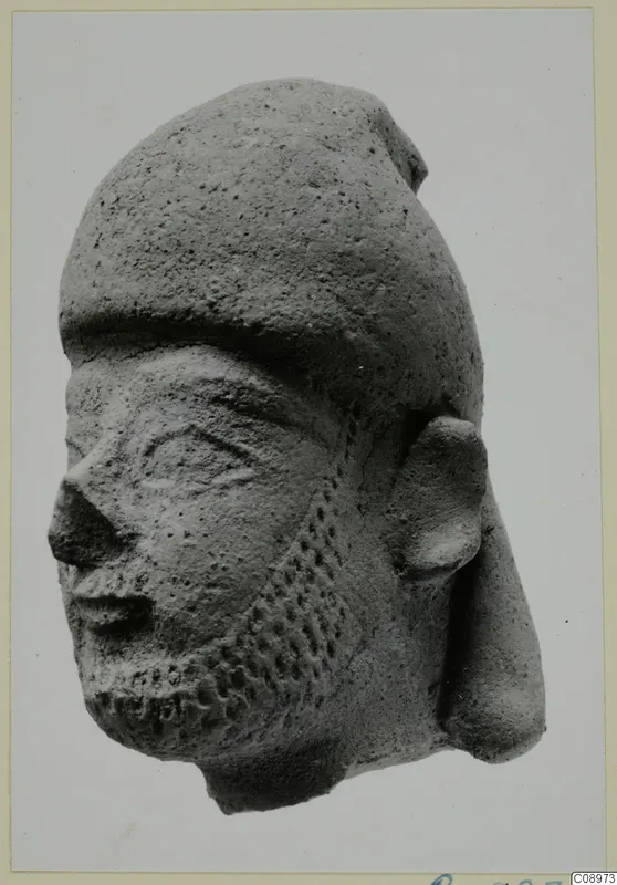 Terracotta Neo-Cypriote head with a dotted beard and a tall, rounded cap, shown in three-quarter view.