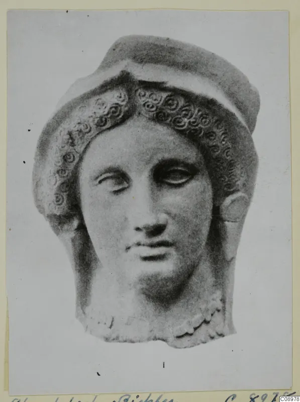 Terracotta head with spiral curls framing the face and a raised band above, on a photo mount