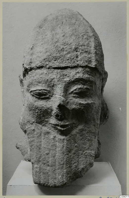 Carved limestone head with a tall headdress and long beard, on a white pedestal, from Kition