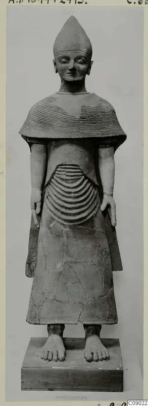 Terracotta statue of a standing figure with a tall conical headdress, a ridged cape and a long robe