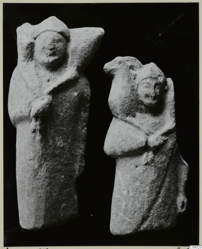 Two limestone figurines of standing figures in draped garments, photographed against a black background
