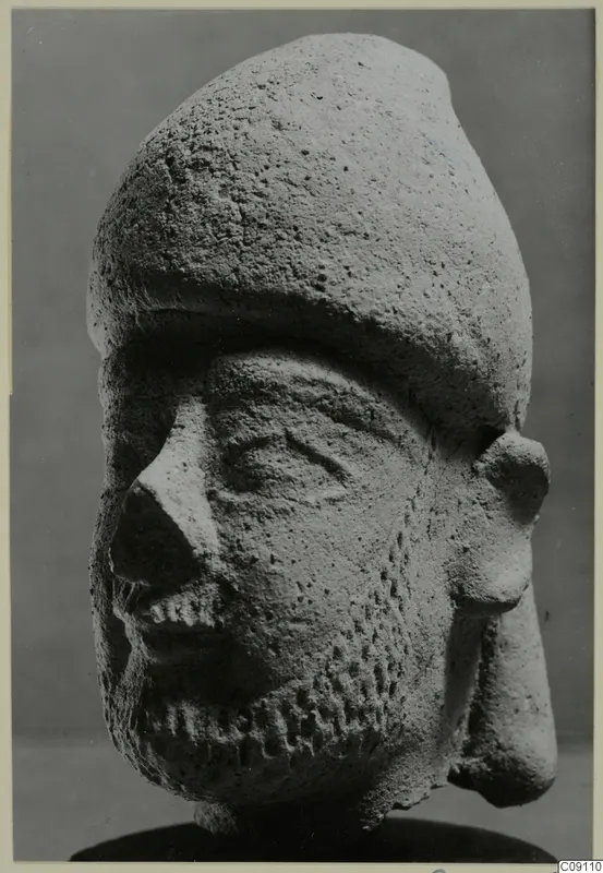 Terracotta head of a bearded figure wearing a tall rounded cap, shown against a plain grey backdrop