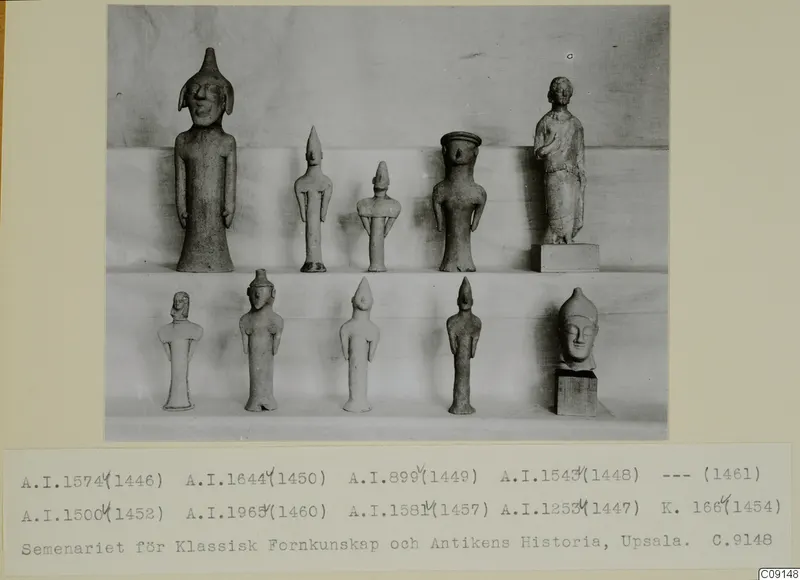 Ten clay statuettes of standing figures arranged on two shelves at Ayia Irini, photographed against a draped cloth.