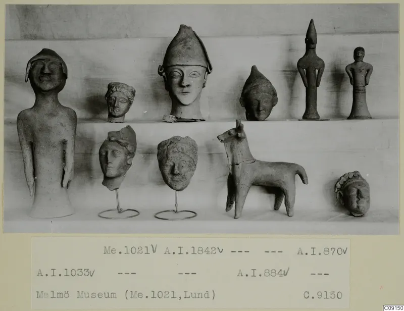 Ten small clay figurines and heads arranged on two shelves, including a standing figure, a capped head and a quadruped figure