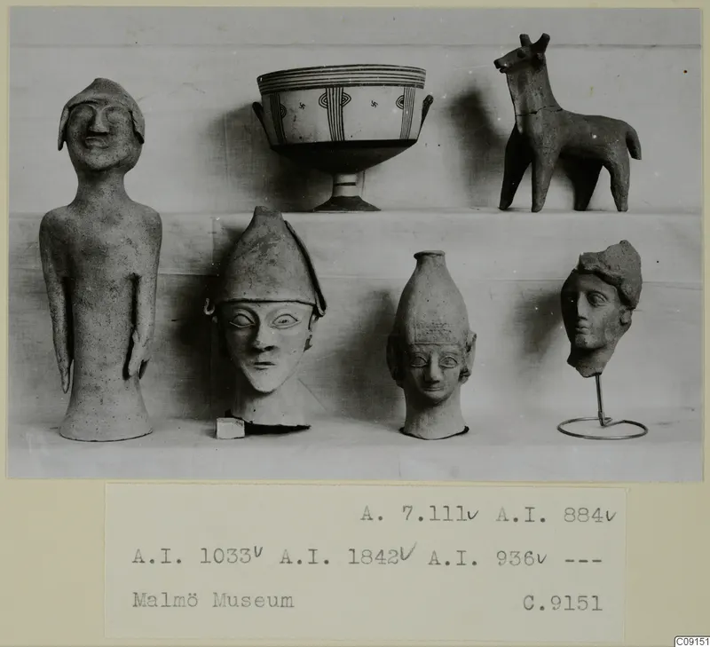 Statues, a footed bowl and an animal figure on a pale cloth, photographed as a print on a card mount.