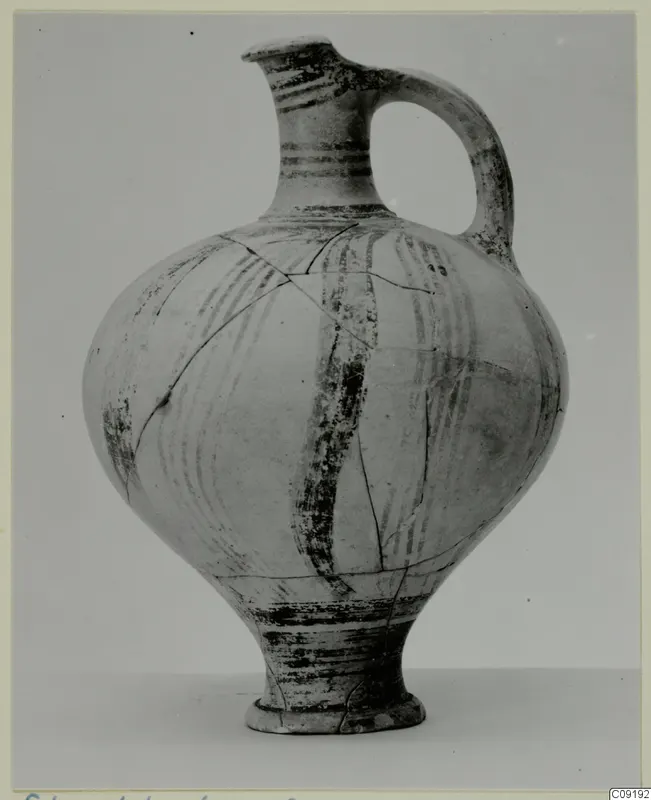 Round-bodied pottery vessel with a narrow neck and strap handle, painted with dark bands, photographed against a grey backdrop