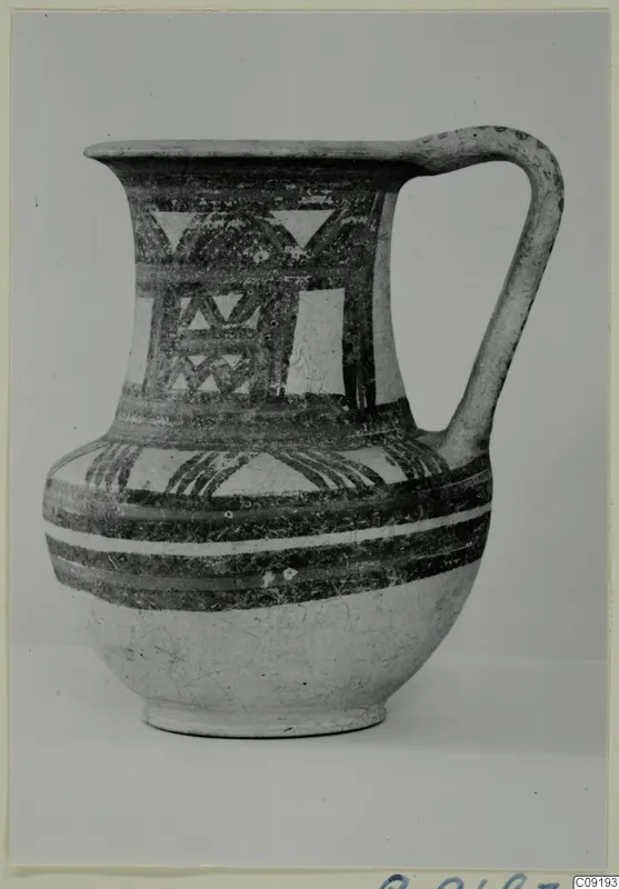 Painted pottery jug with a single handle, banded and triangular patterns in dark paint on a pale body.