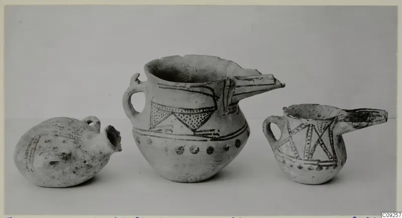 Three painted pottery vessels with spouts and handles, shown side by side against a plain grey background.