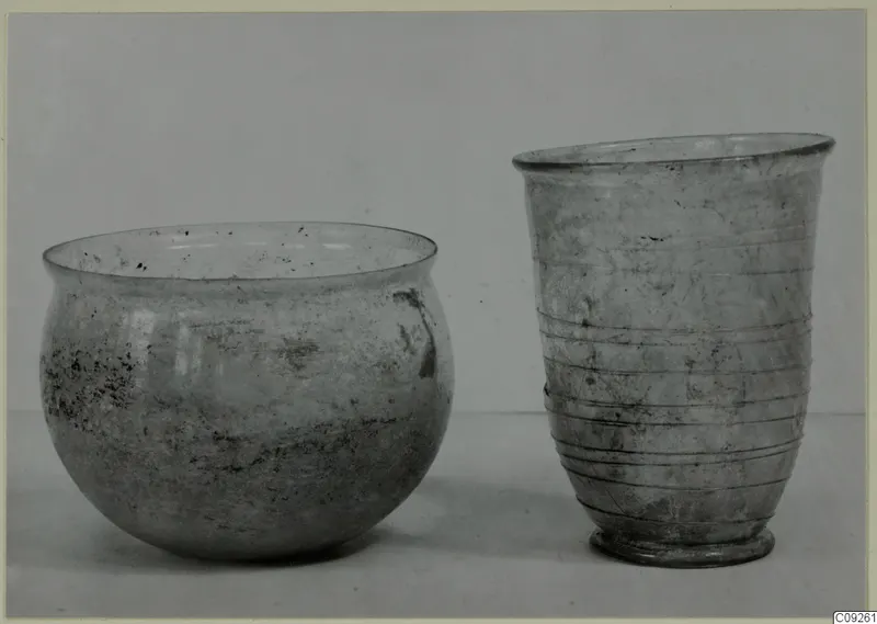Two blown glass vessels: a rounded bowl on the left and a ribbed beaker on the right, on a plain surface