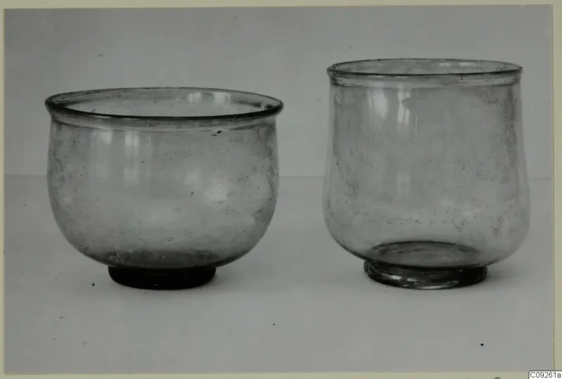 Two glass vessels side by side, one wide and rounded on the left, one taller on the right.