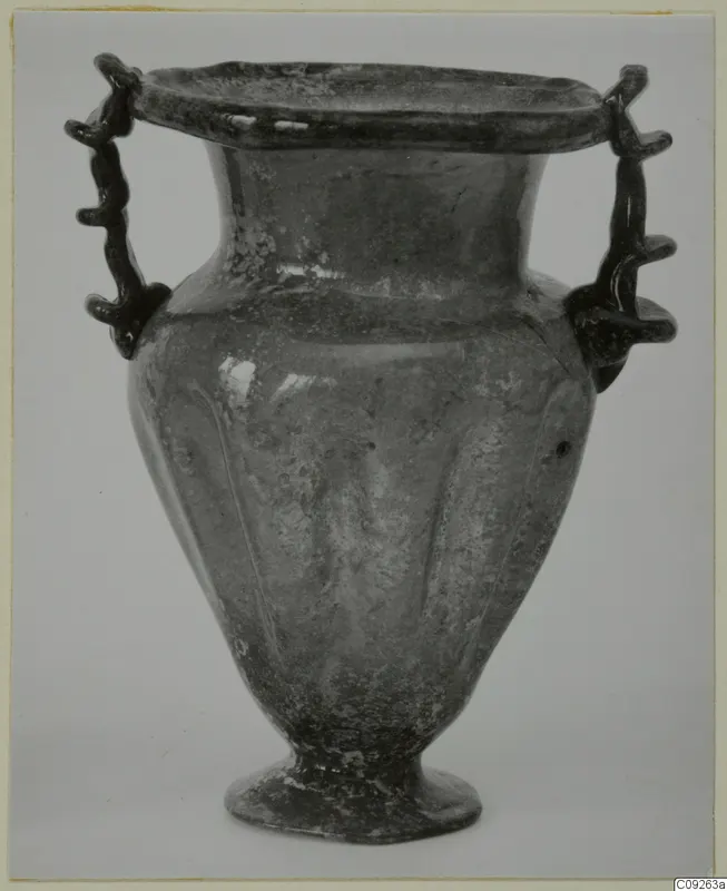 Blown glass vessel with two trailed handles, a flared rim and a ribbed body, shown against a pale background