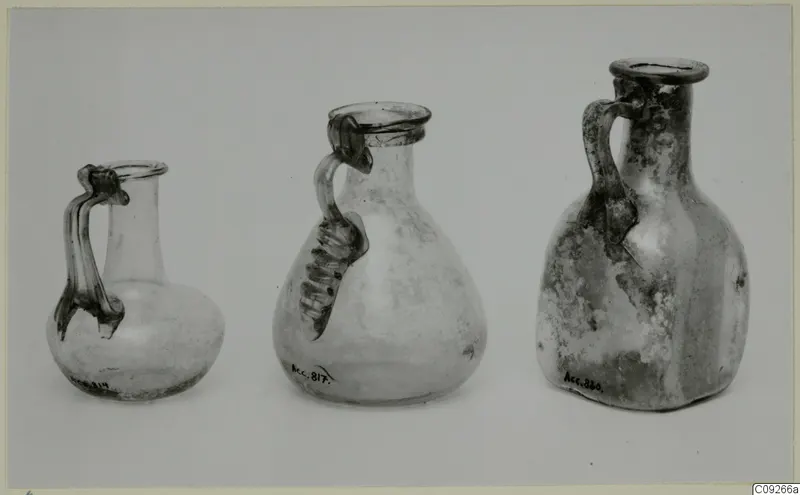 Three handled blown glass jugs shown side by side on a pale surface.