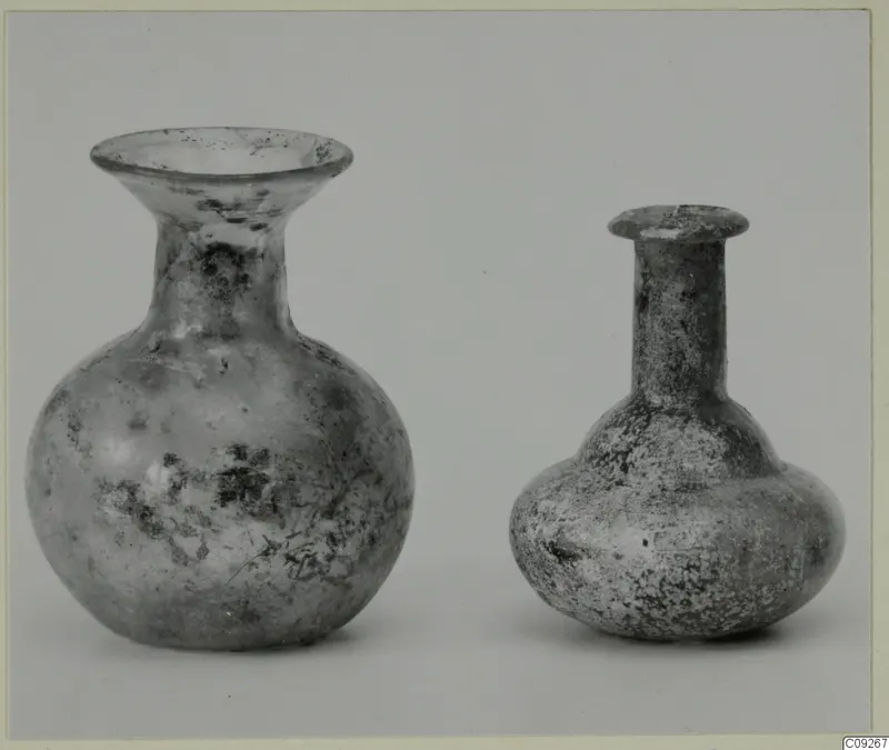 Two small blown glass vessels, one with a wide flared mouth and one with a long narrow neck, on a grey background.
