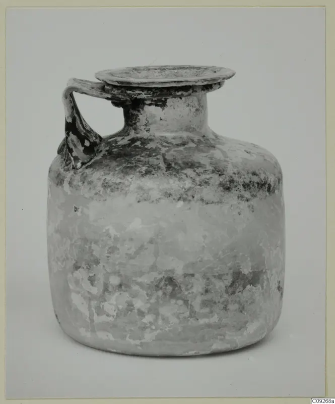 Blown glass jug with a single handle and a flared rim, photographed against a plain grey background