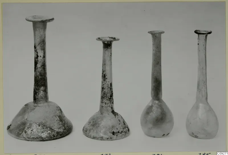 Four blown glass bottles with long necks and flared rims, shown side by side against a plain background.