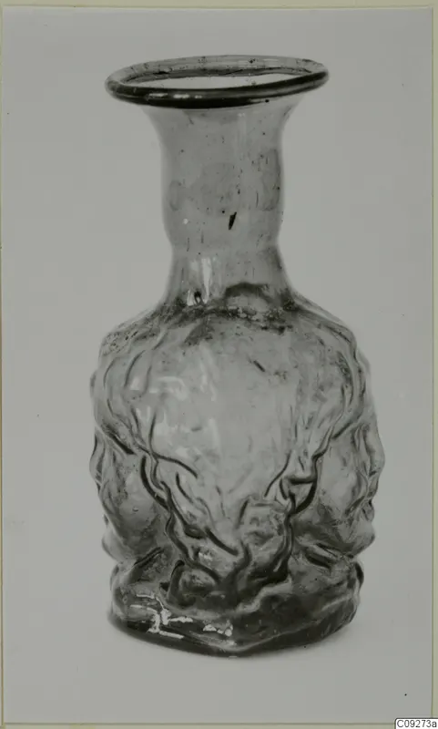 Blown glass vessel with a flared neck and moulded faces on its body