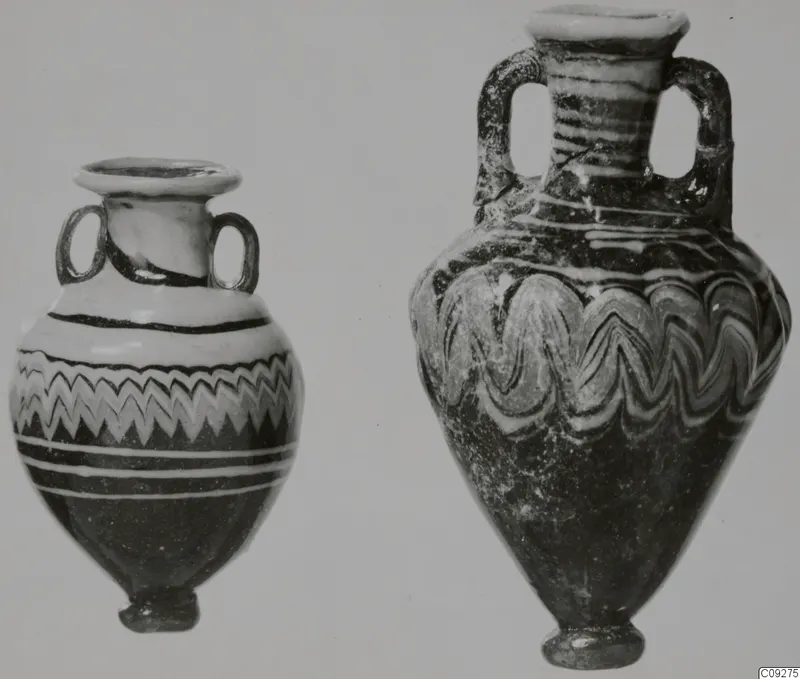 Two sand-core glass vessels, each with two loop handles; the left has a zigzag band, the right looping white trails